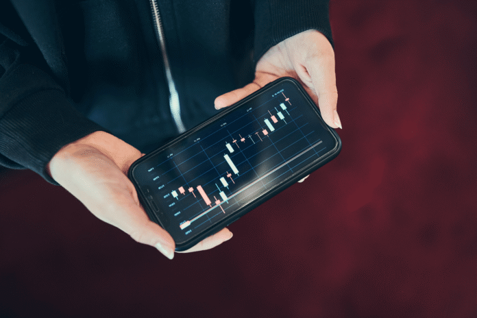 Ruka drži telefon sa prikazom kripto grafikona